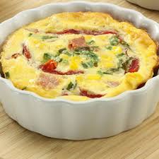 A creamy quiche with spinach and ham in a white ceramic dish.