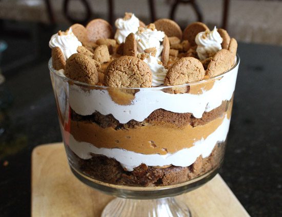 Layered pumpkin dessert with whipped cream and cookie topping in a glass bowl.