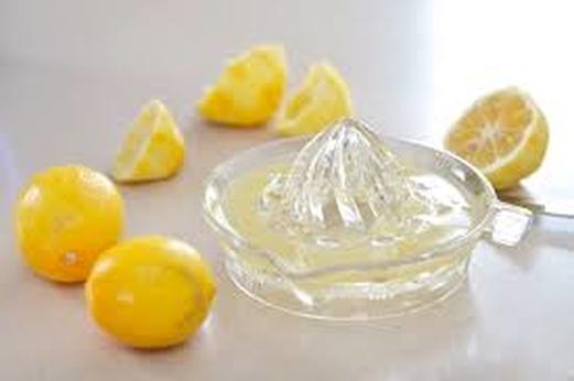Glass lemon squeezer with fresh lemons on table.