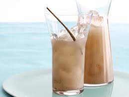 Two iced coffee drinks with straws on a table by the sea.