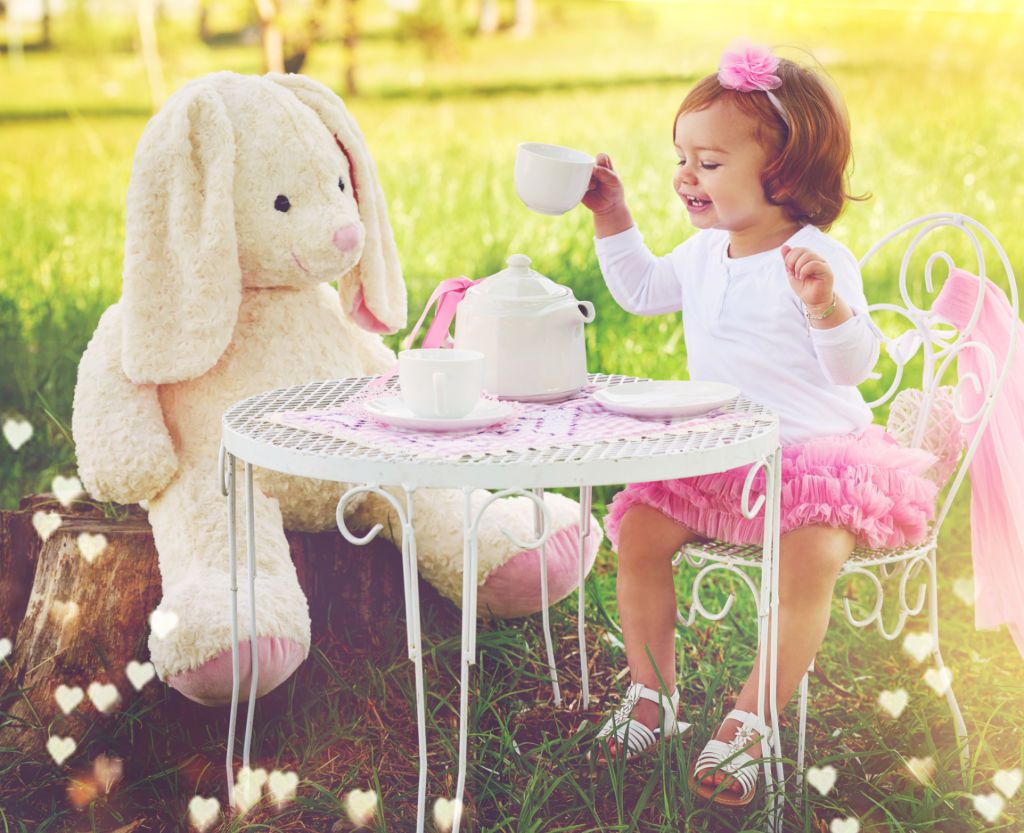 A little girl having a tea party with a large stuffed bunny outdoors.