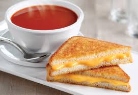 Grilled cheese sandwich with tomato soup on a white plate.