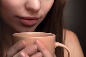 Woman holding a cup close to her lips, about to drink.