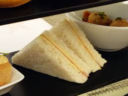 Triangular sandwiches with a creamy filling on a black tray.
