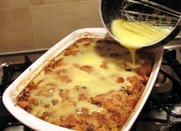 Pouring custard over a baked bread pudding in a white dish.