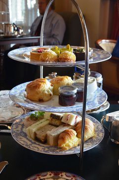 Three-tiered stand with scones, sandwiches, and desserts for afternoon tea.