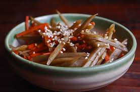 A bowl of seasoned burdock root sticks topped with sesame seeds.