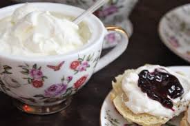 A vintage floral teacup filled with cream, next to a scone topped with cream and jam.