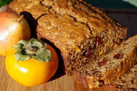 A close-up of a slice of nutty, fruity bread with a persimmon beside it.