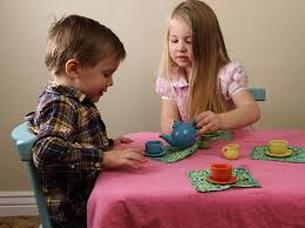 Two children playing tea party with toy dishes at a pink table.