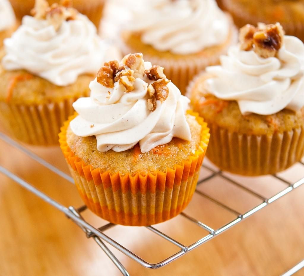 Cupcakes topped with whipped cream and walnuts on a cooling rack.