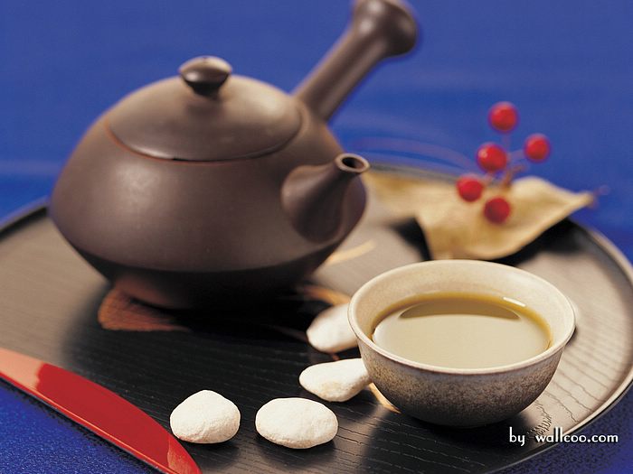 A traditional teapot with a cup of tea and marshmallows on a dark surface.