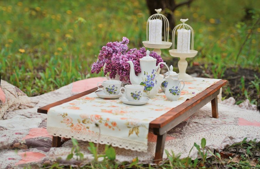 Outdoor tea setup with lilac flowers and vintage teapot on a rustic table.