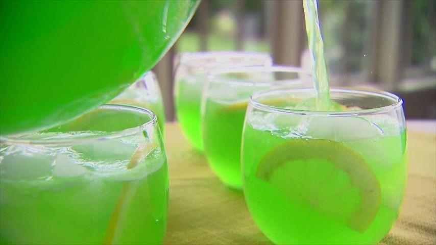 Refreshing green lime drinks being poured into glasses outdoors.