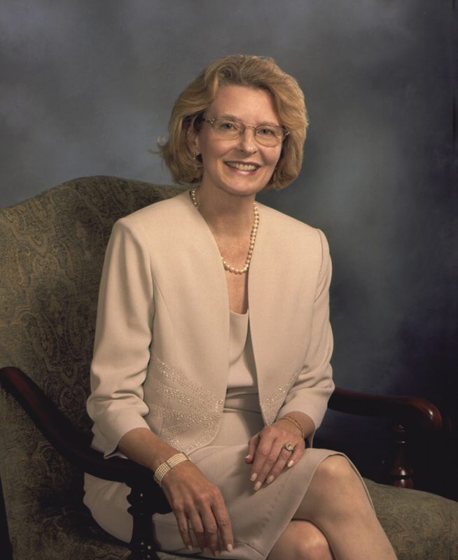A professional woman seated on a chair, smiling at the camera.