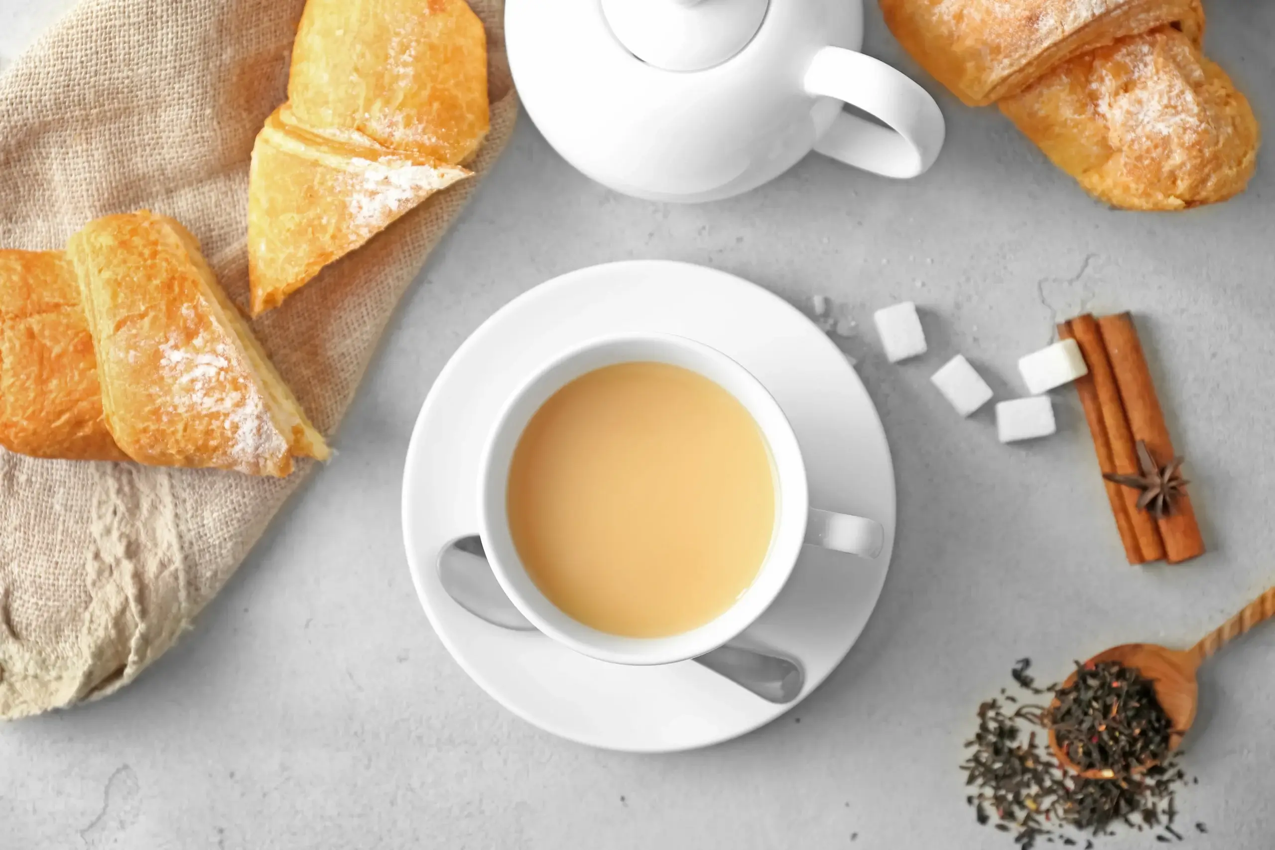 Cup of tea with croissants and sugar cubes on a gray surface.