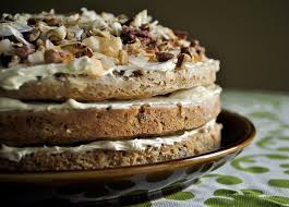 A close-up of a layered cake with creamy frosting and nut toppings.