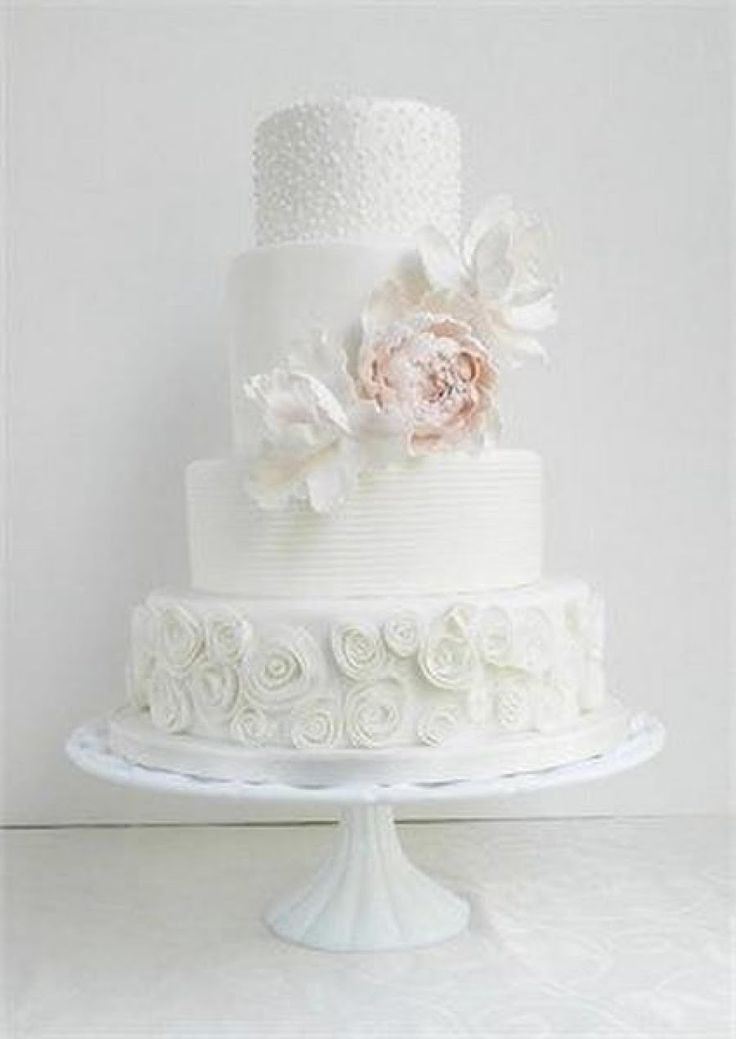 Elegant white three-tier cake with floral decorations and a blush pink flower.