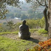 Person sitting alone on a grassy hill overlooking a scenic valley.