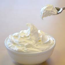 A bowl filled with fluffy whipped cream and a spoon lifting some.