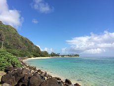 A serene beach with clear turquoise water and rocky shoreline under a blue sky.