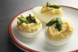 Deviled eggs topped with asparagus spears on a white plate.