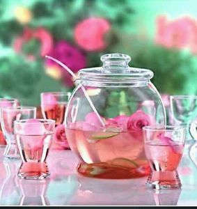 Glass teapot and cups with rose tea on a pink table.