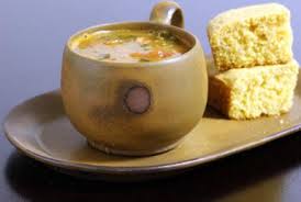 Rustic ceramic mug filled with soup, accompanied by cornbread.