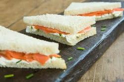 Triangular smoked salmon finger sandwiches on a slate board.