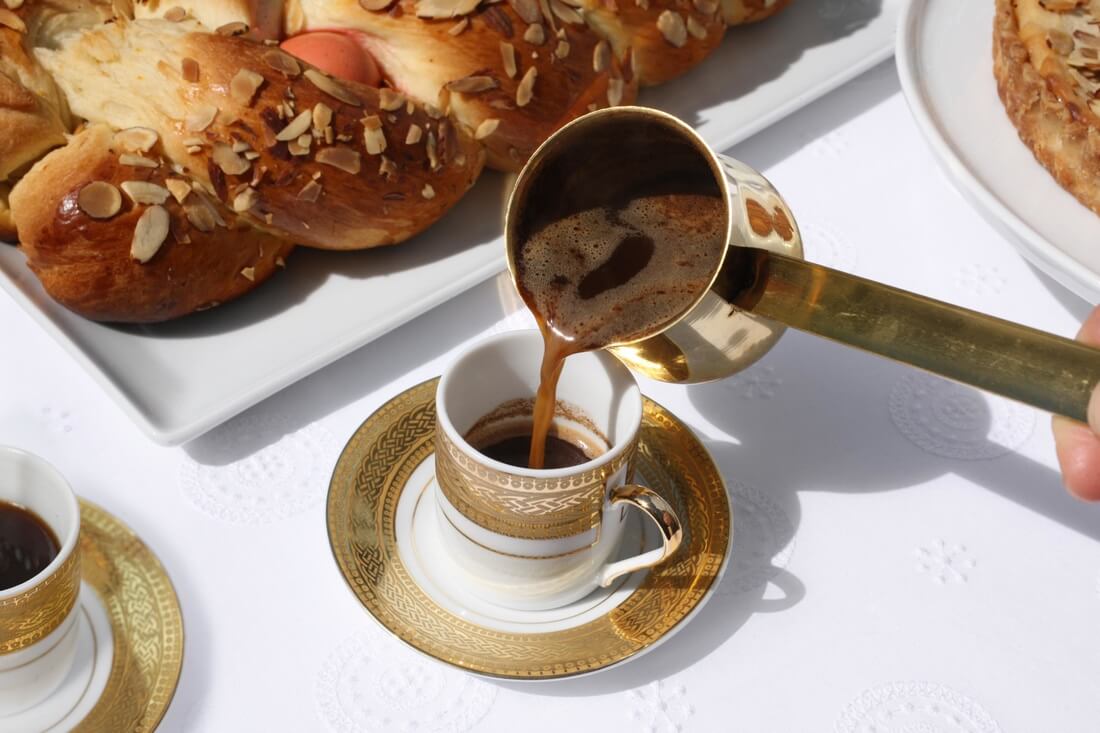 Pouring Turkish coffee into a small cup beside pastries.