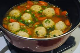 A bowl of vegetable soup with meatballs and herbs.