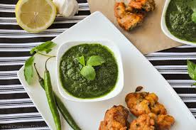 A bowl of green chutney with fried snacks and green chili on the side.