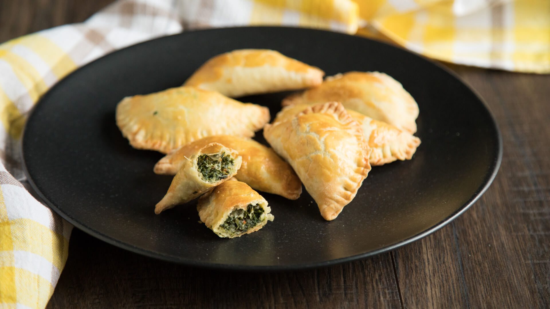 Golden baked spinach and cheese hand pies on a black plate.