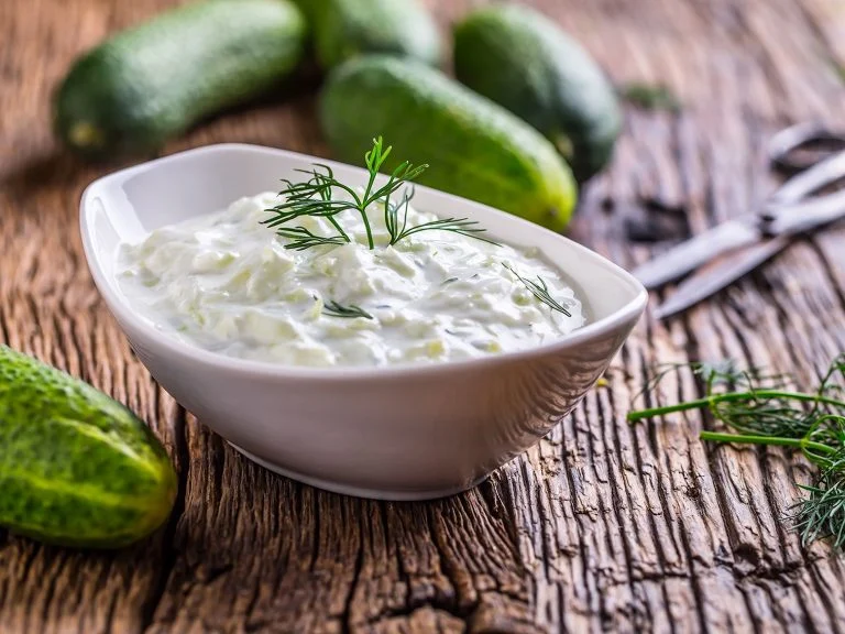A bowl of creamy tzatziki sauce garnished with dill on a wooden table.