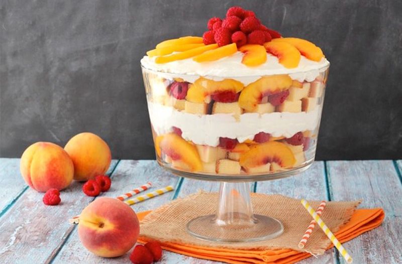 Peach and raspberry layered dessert in a glass trifle bowl.