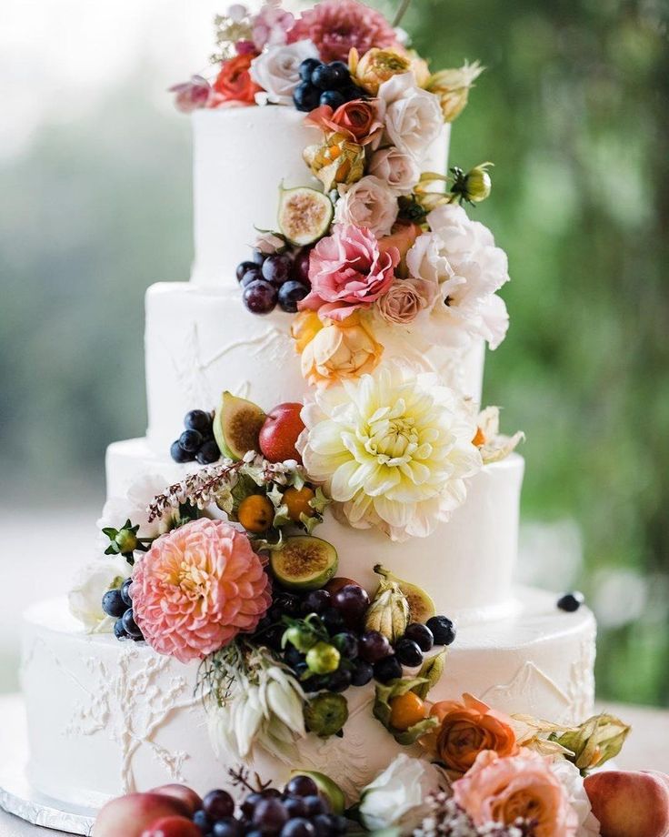 Elegant white wedding cake adorned with cascading fresh flowers in soft pastel hues.