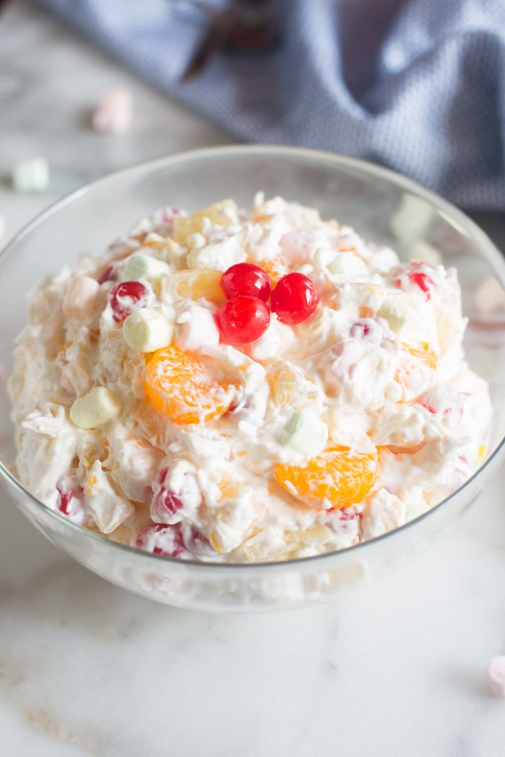 A bowl of creamy fruit salad with cherries and mandarin oranges.