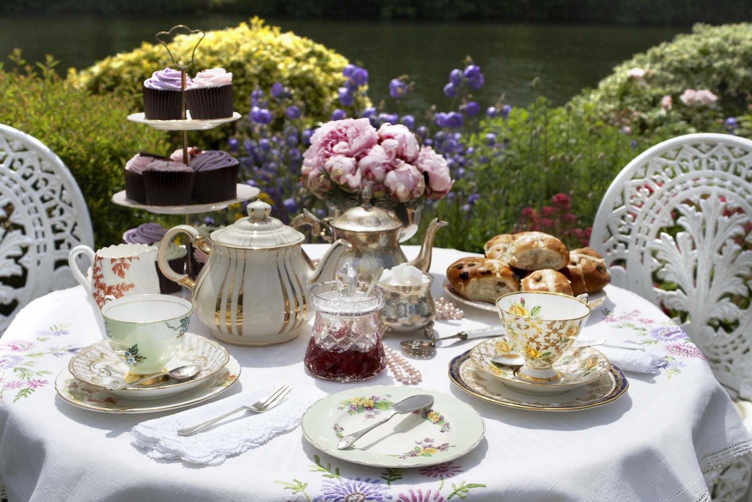 Elegant outdoor tea party setup with fine china and fresh flowers.