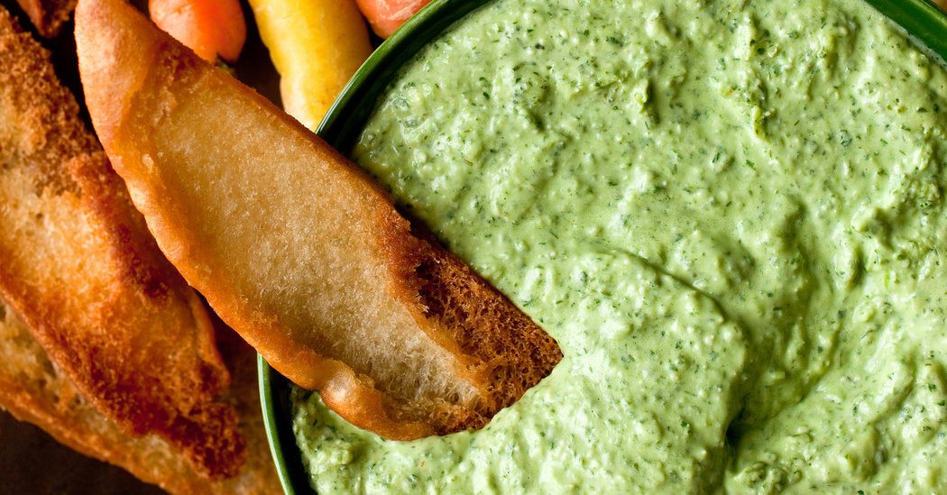 A piece of bread dipped in creamy green spinach dip.