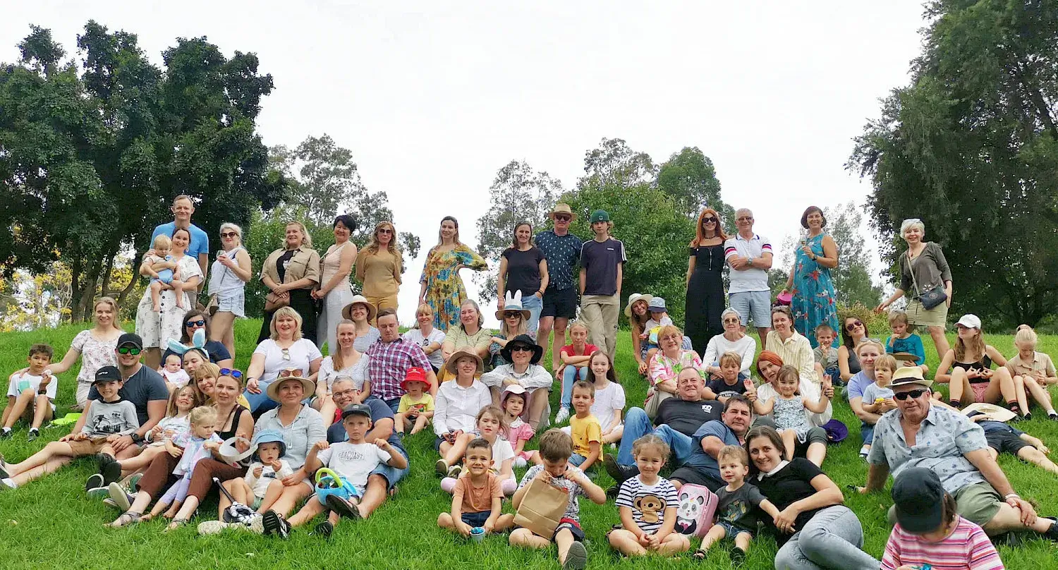Large group of adults and children posing outdoors on a grassy hill.