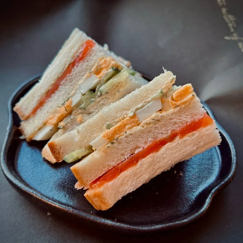 Three triangular sandwiches with layers of vegetables and egg on a black plate.