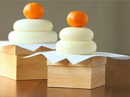 Traditional Japanese kagami mochi with mandarin oranges on wooden stands.