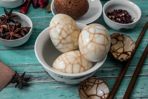 Three marbled eggs in a white bowl on a turquoise wooden table.