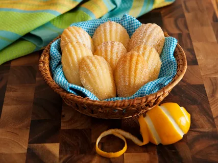 Golden madeleine cookies in a basket with a blue cloth.