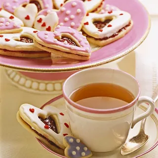Tea cup with heart-shaped cookies on a pink plate.