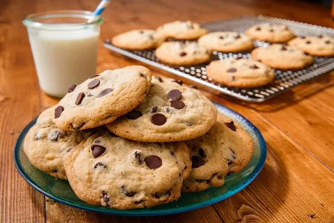 Freshly baked chocolate chip cookies on a plate beside a glass of milk.