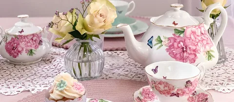 Elegant tea set with floral patterns and fresh roses on a lace tablecloth.