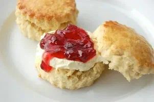 A biscuit topped with cream and strawberry jam.