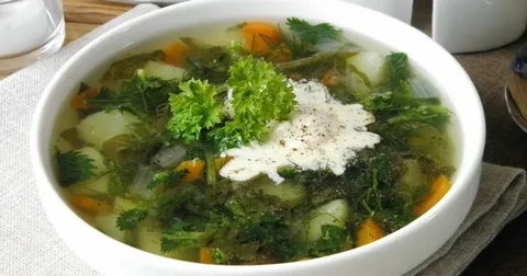 A bowl of vegetable soup garnished with herbs and a dollop of cream.
