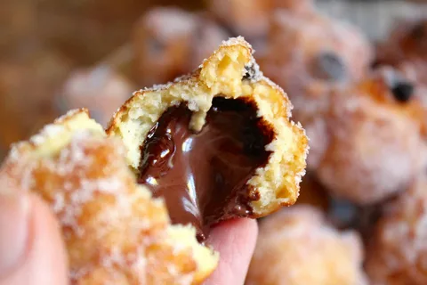 Close-up of a hand holding a sugar-coated doughnut filled with melted chocolate.